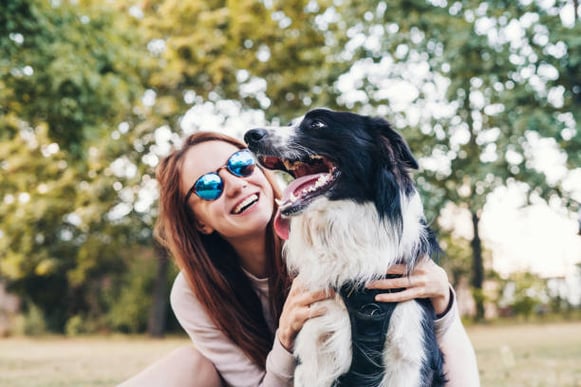 A woman wearing sunglasses hugs her dog outside