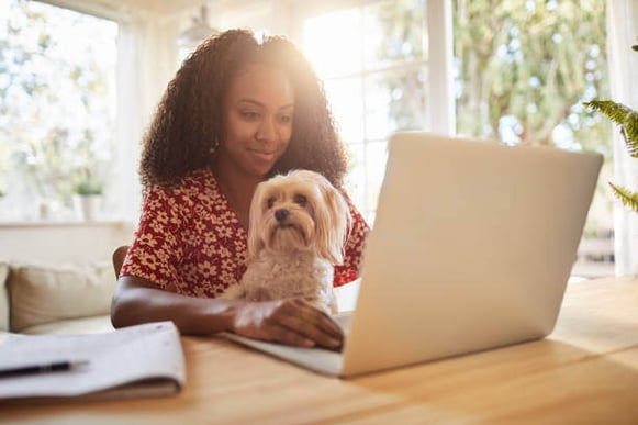 A woman uses a laptop as a dog sits on her lap