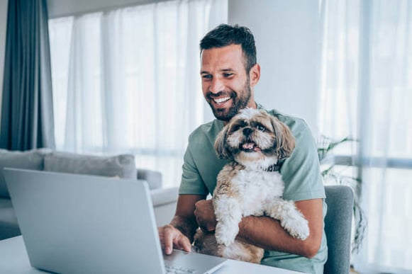 A man uses a laptop as a dog sits on his lap