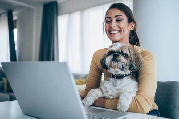 A woman uses a laptop as a dog sits on her lap