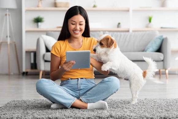 A woman uses an iPad as her dog sits next to her