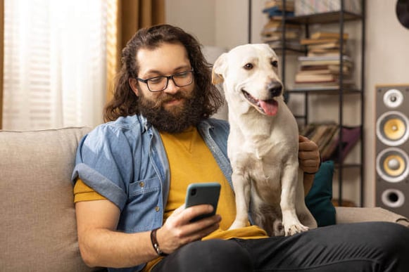 A man uses a cell phone while holding a dog