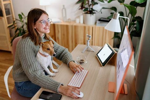 A woman uses a computer as a dog sits on her lap