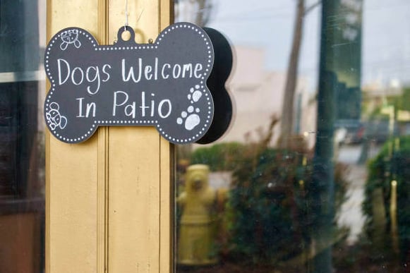 A sign that says "Dogs Welcome in Patio" hangs outside