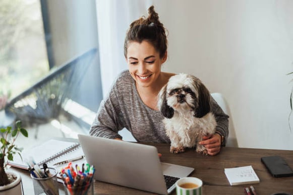 A woman uses a laptop as a dog sits on her lap