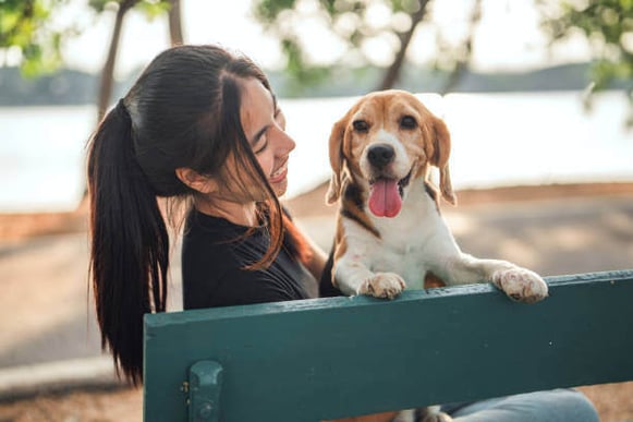 A woman and dog sit on a bench outside